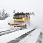 Aura-auto työntää lunta pöllyävässä lumessa.