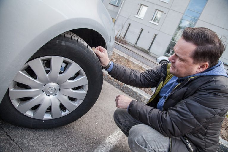 Henkilö tarkastaa renkaiden urasyvyyksiä