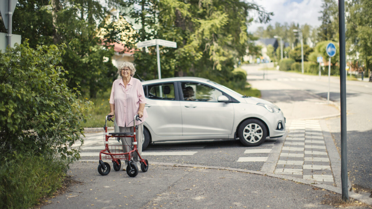 Ikääntynyt suojatien ylittäjä rollaattorin kanssa.