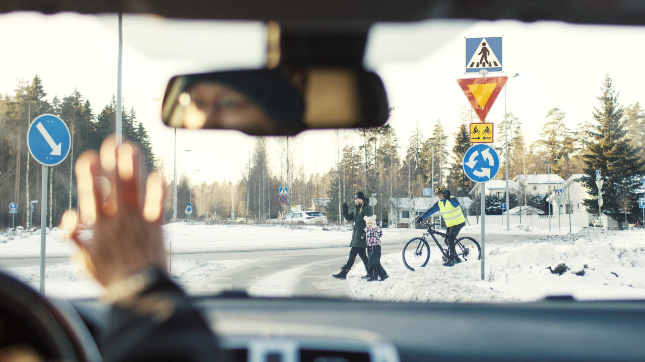 Auton tuulilasin läpi liikenneympyrässä suojatietä ylittävät jalankulkijat ja pyöräilijä.