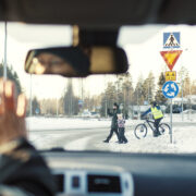 Auton tuulilasin läpi liikenneympyrässä suojatietä ylittävät jalankulkijat ja pyöräilijä.