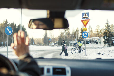 Auton tuulilasin läpi liikenneympyrässä suojatietä ylittävät jalankulkijat ja pyöräilijä.